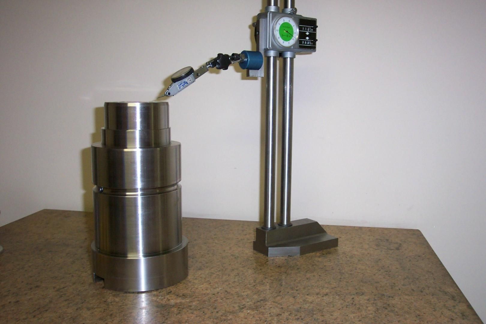 Un indicateur de test sur un comparateur de hauteur mesurant la surface supérieure d'une pièce métallique cylindrique sur une surface plane.