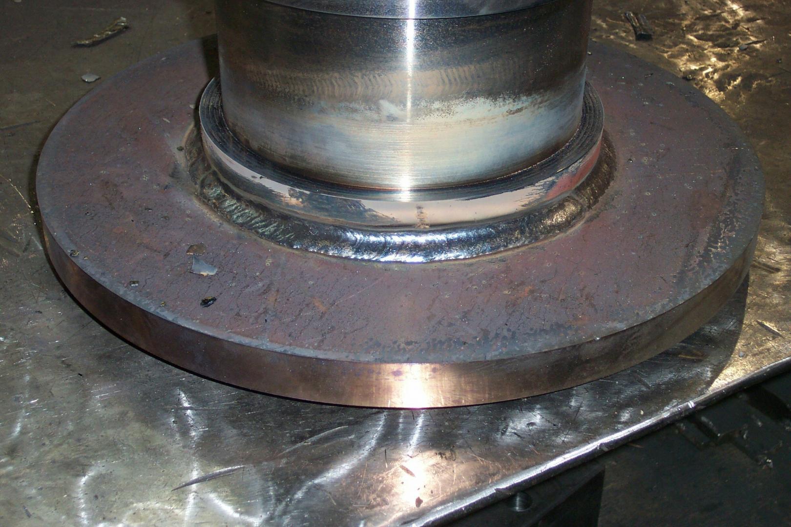 A metal shaft is welded to a circular steel plate, showing a circular bead of weld along the connection point.