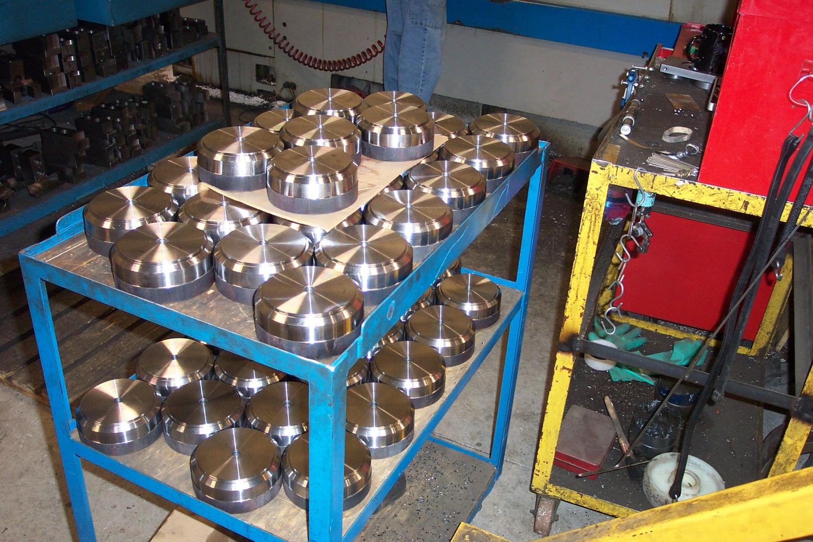 Dans un atelier, un chariot métallique à deux étagères permet de ranger de nombreux composants industriels métalliques circulaires empilés.