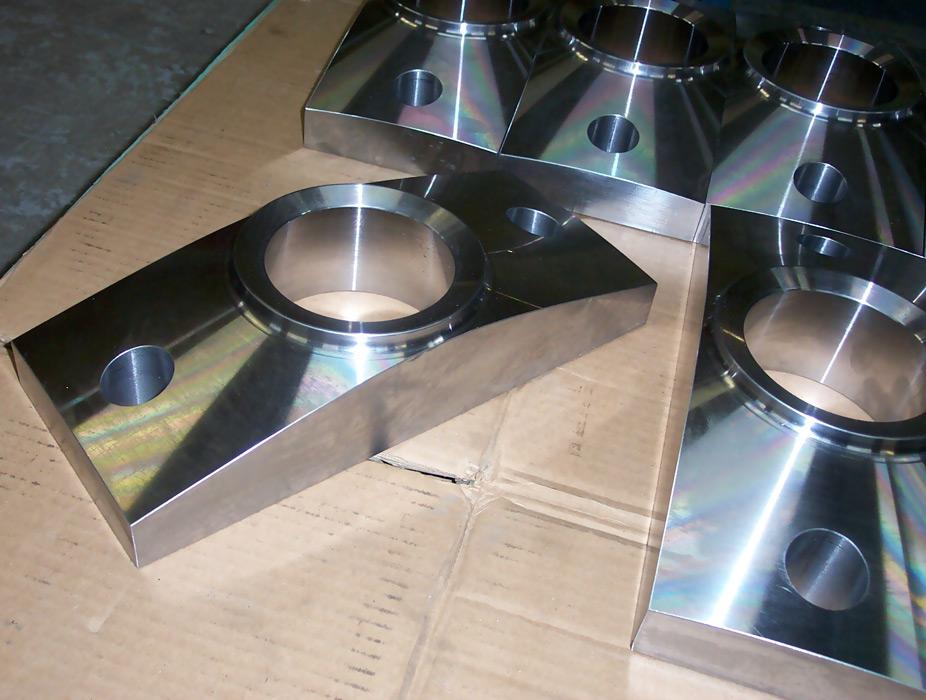 Several machined, polished steel rectangular blocks with circular cutouts resting on a cardboard surface.
