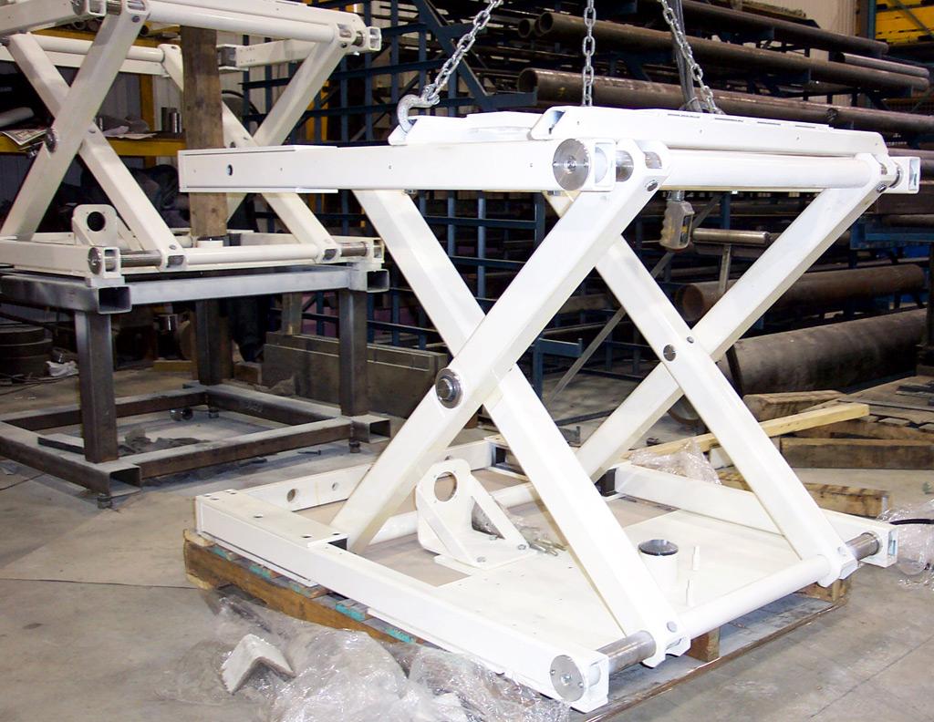 Two white, industrial scissor-lift metal frames on wooden pallets in a workshop.