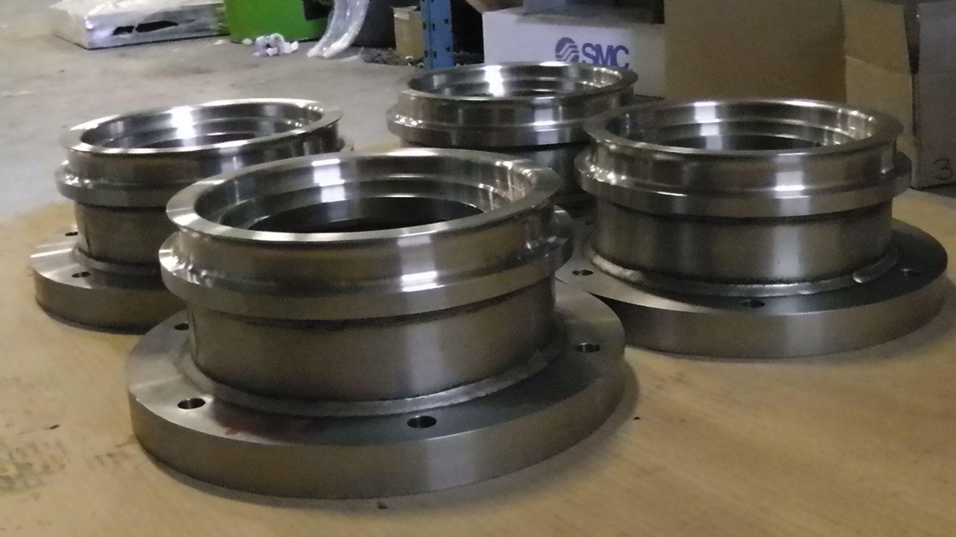 Quatre pièces métalliques cylindriques de machines, munies de bases à brides, reposent sur une surface dans un environnement industriel.