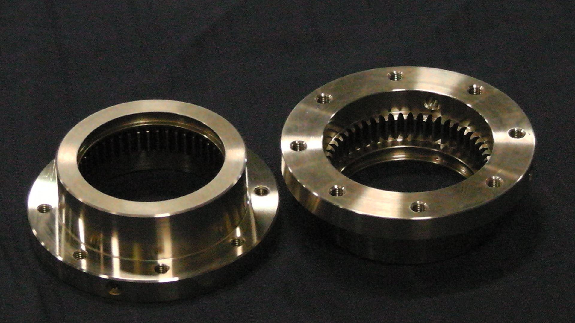 Deux pièces mécaniques métalliques circulaires, dotées de dents d'engrenage internes et de trous de boulons, reposant sur une surface sombre.