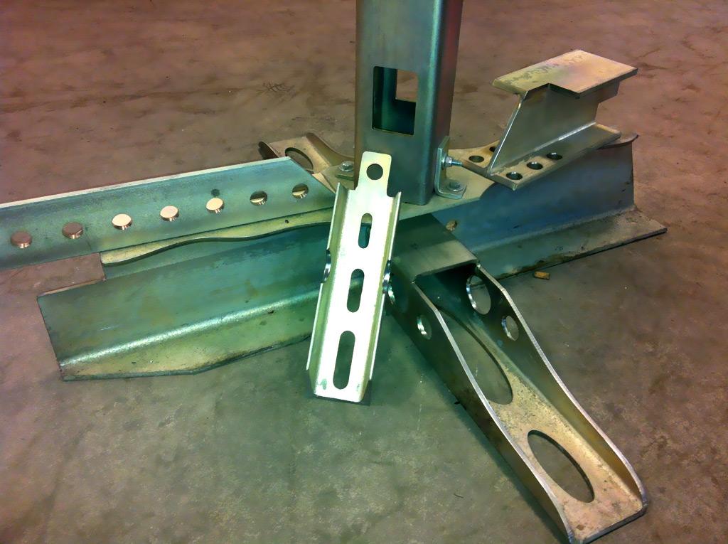 A collection of galvanized metal structural components and brackets arranged on a concrete floor.
