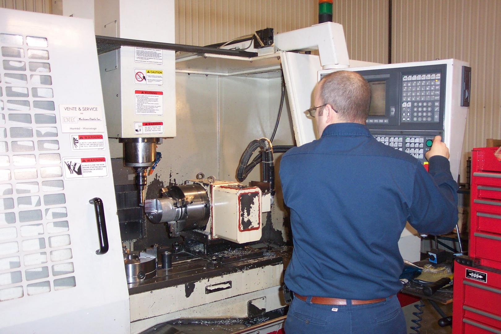 Une personne en chemise bleue utilise une fraiseuse CNC dans un atelier.