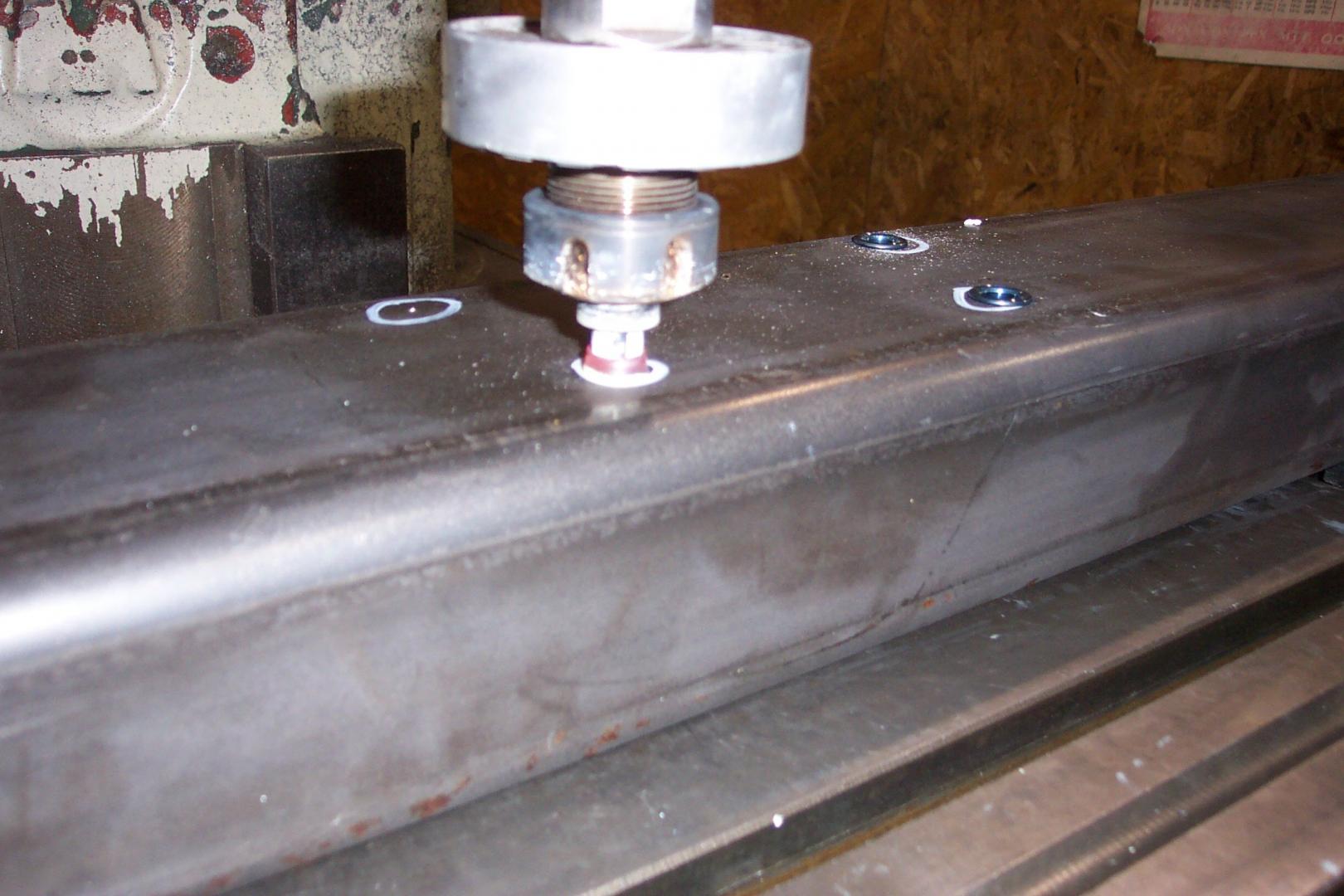 A metal machining tool drills holes into a steel beam, showing fresh markings on the surface.