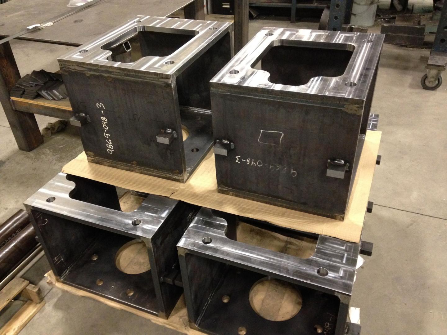 Quatre éléments de structure en acier industriel reposent sur une palette en bois à l'intérieur d'un atelier.