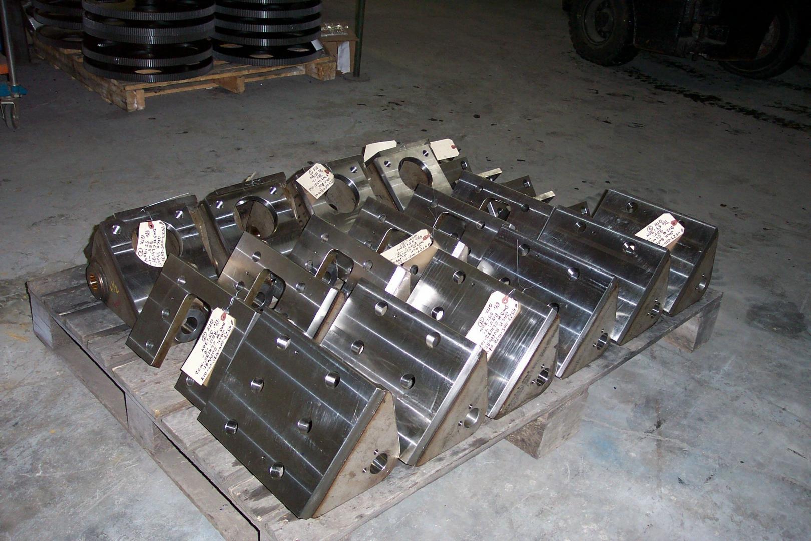 A pallet holding several dark, angular metal industrial components in a warehouse setting.