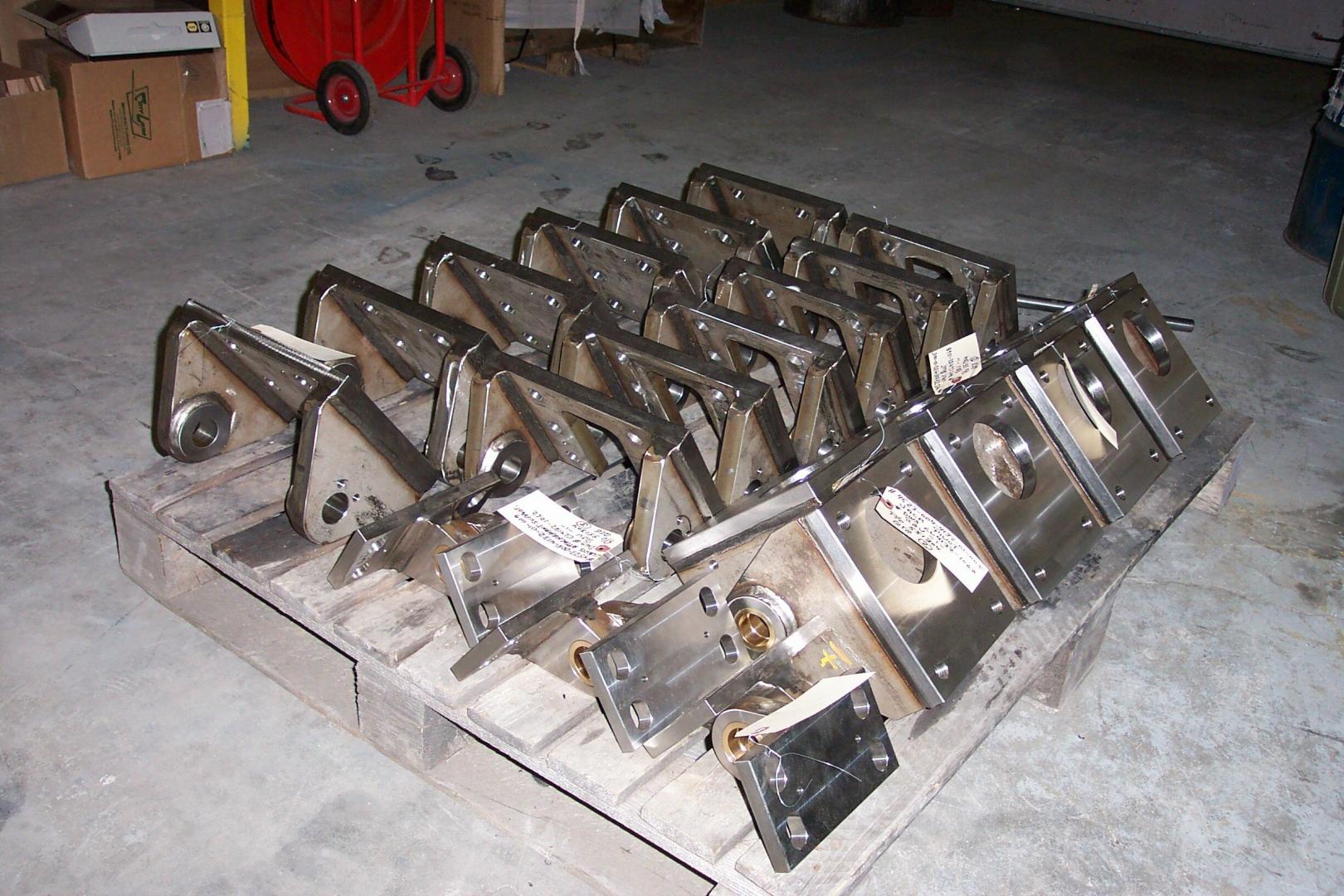 A wooden pallet loaded with several identical, L-shaped industrial steel metal brackets in a warehouse setting.