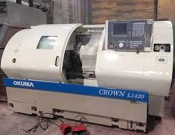 Un tour à commande numérique Okuma Crown L1420 blanc avec une bande décorative bleue, posé sur un sol en béton.