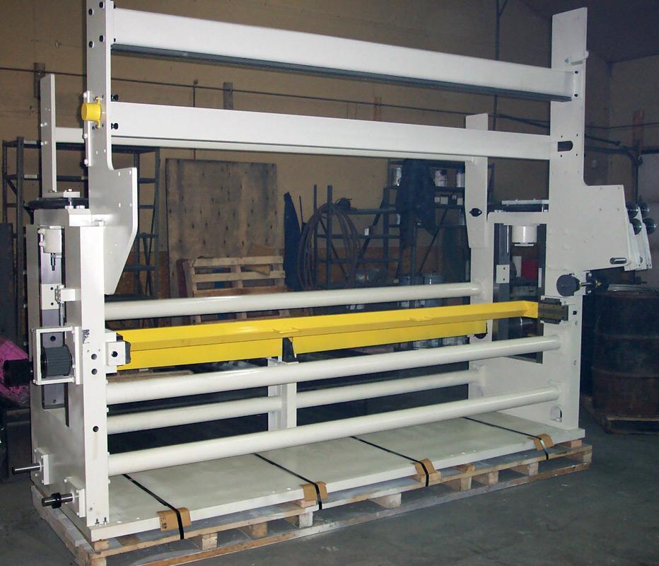 A large, white industrial textile machine frame featuring a horizontal yellow bar, resting on a wooden pallet in a warehouse.