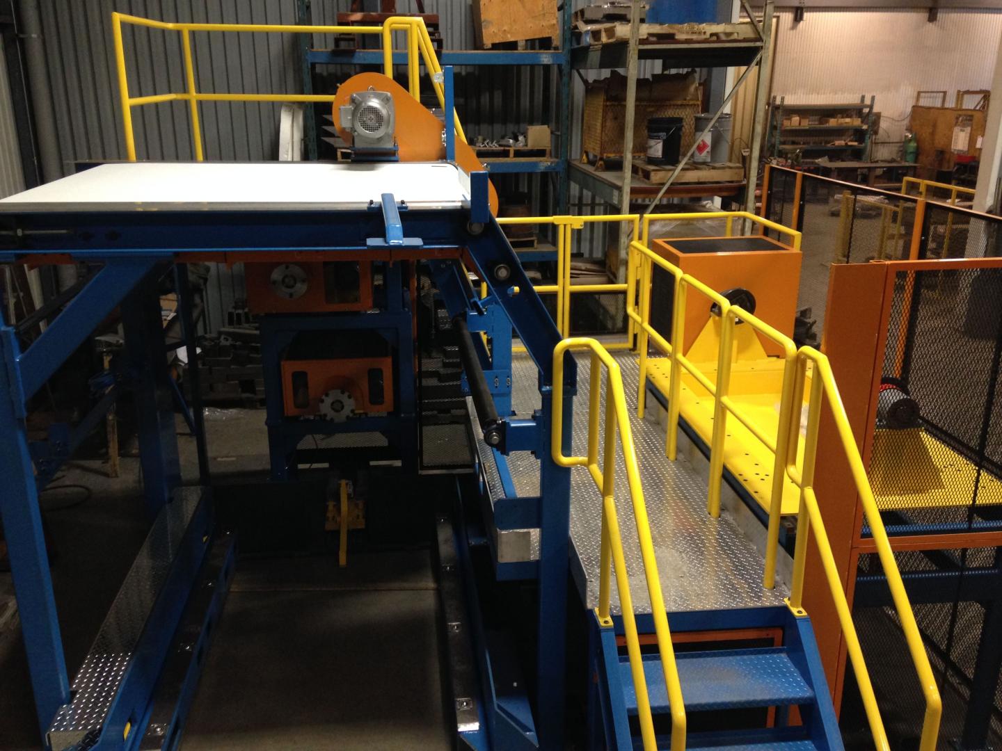 Industrial machinery featuring a blue and orange frame, a platform with yellow railings, and metal stairs in a factory.