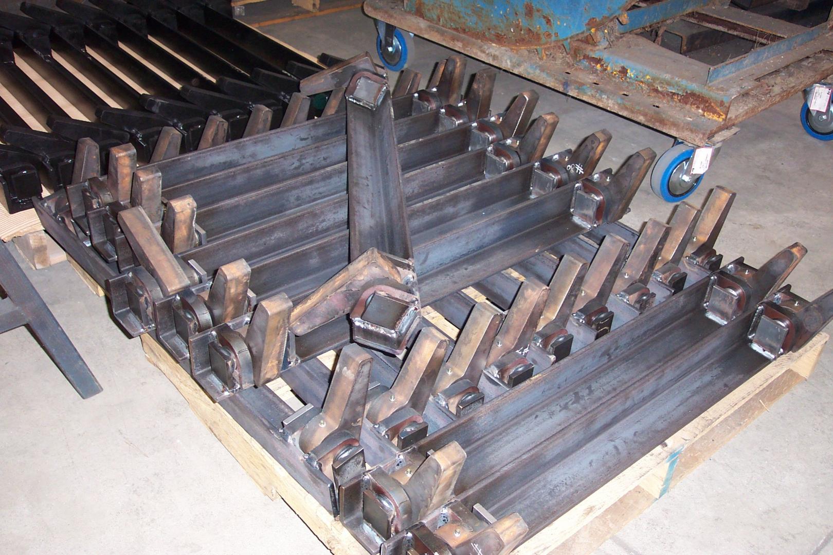 A pallet of industrial steel parts with evenly spaced, angled metal teeth arranged on a concrete shop floor.