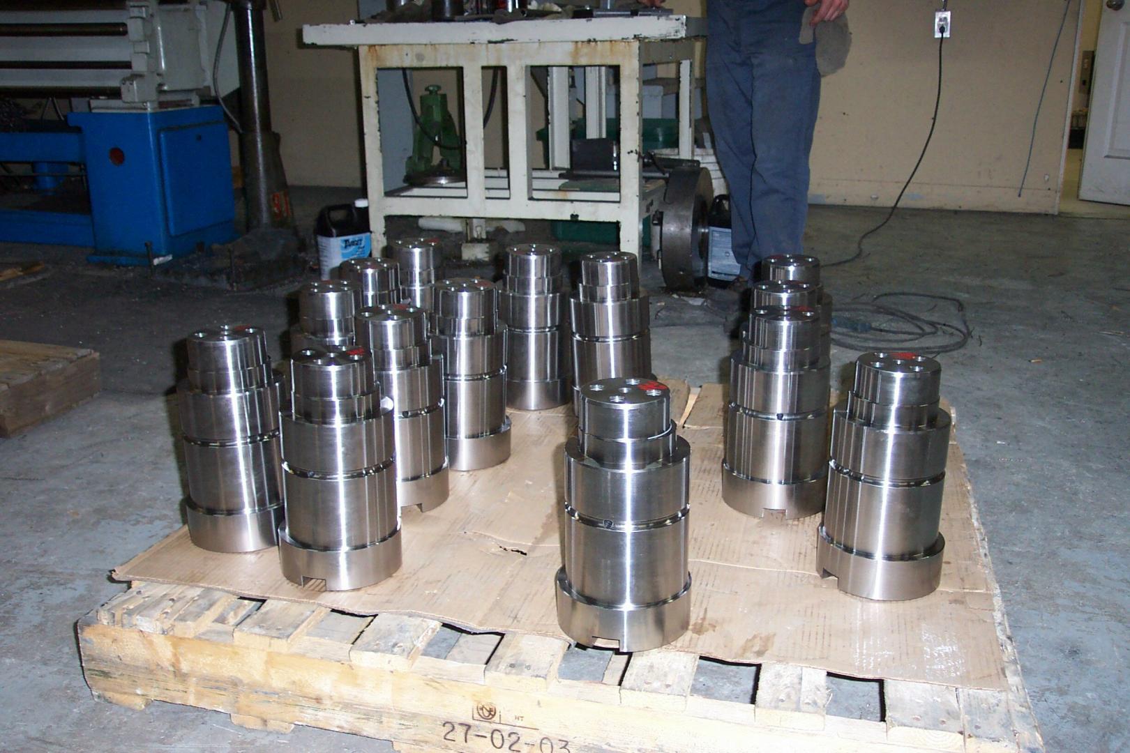 Plusieurs pièces cylindriques en acier usiné sont disposées sur une palette en bois dans un atelier.