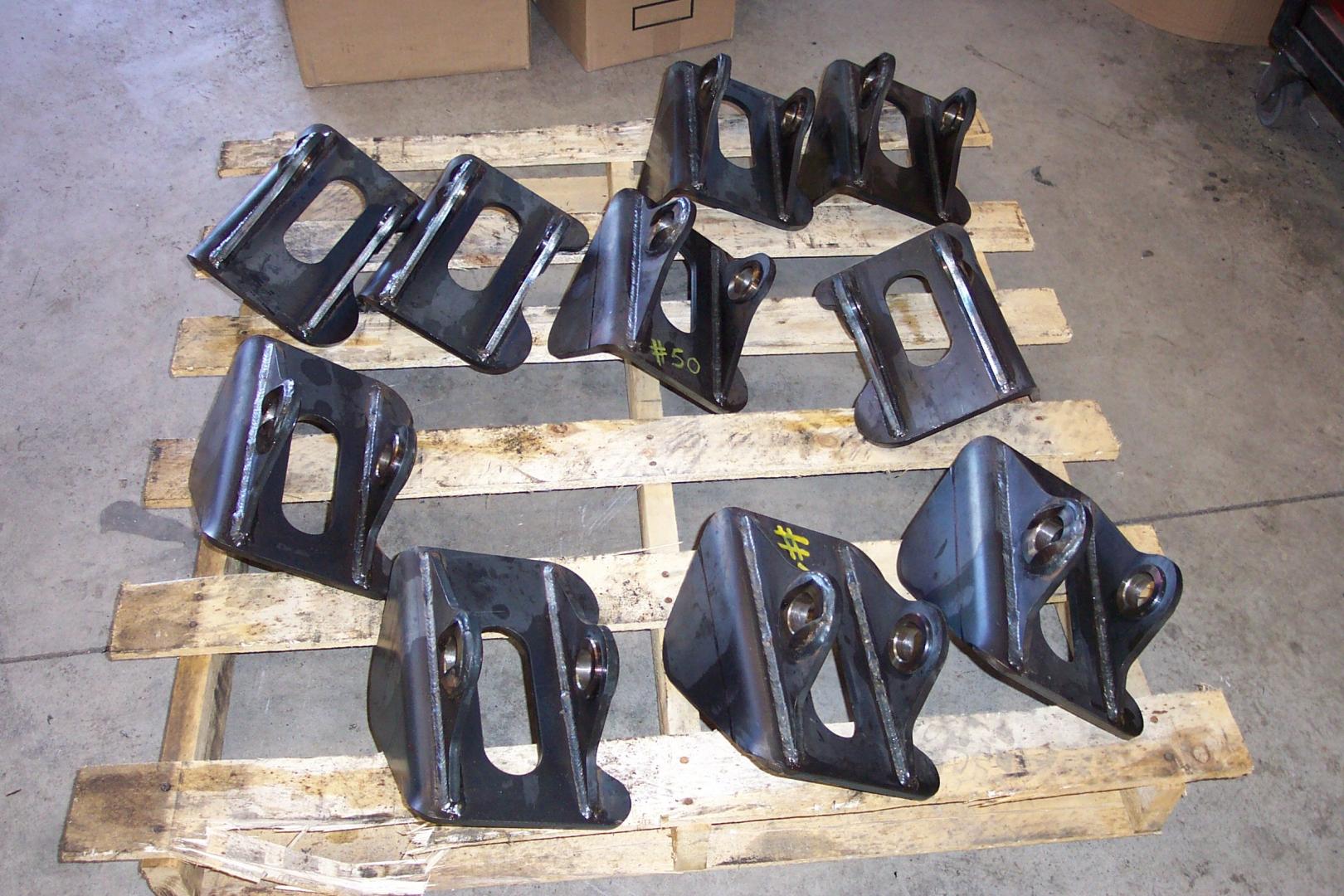 Ten identical black metal mechanical brackets arranged on a wooden shipping pallet.
