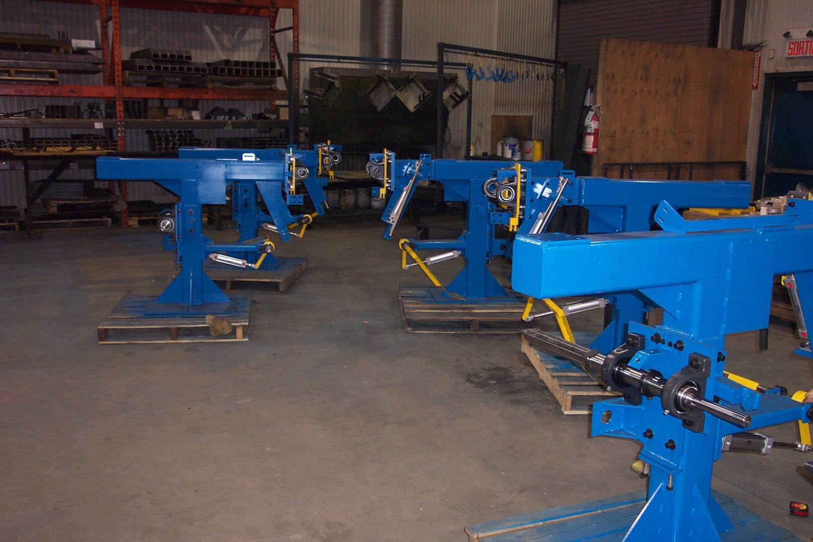 Three bright blue heavy-duty industrial assembly stands arranged in a workshop on wooden pallets.