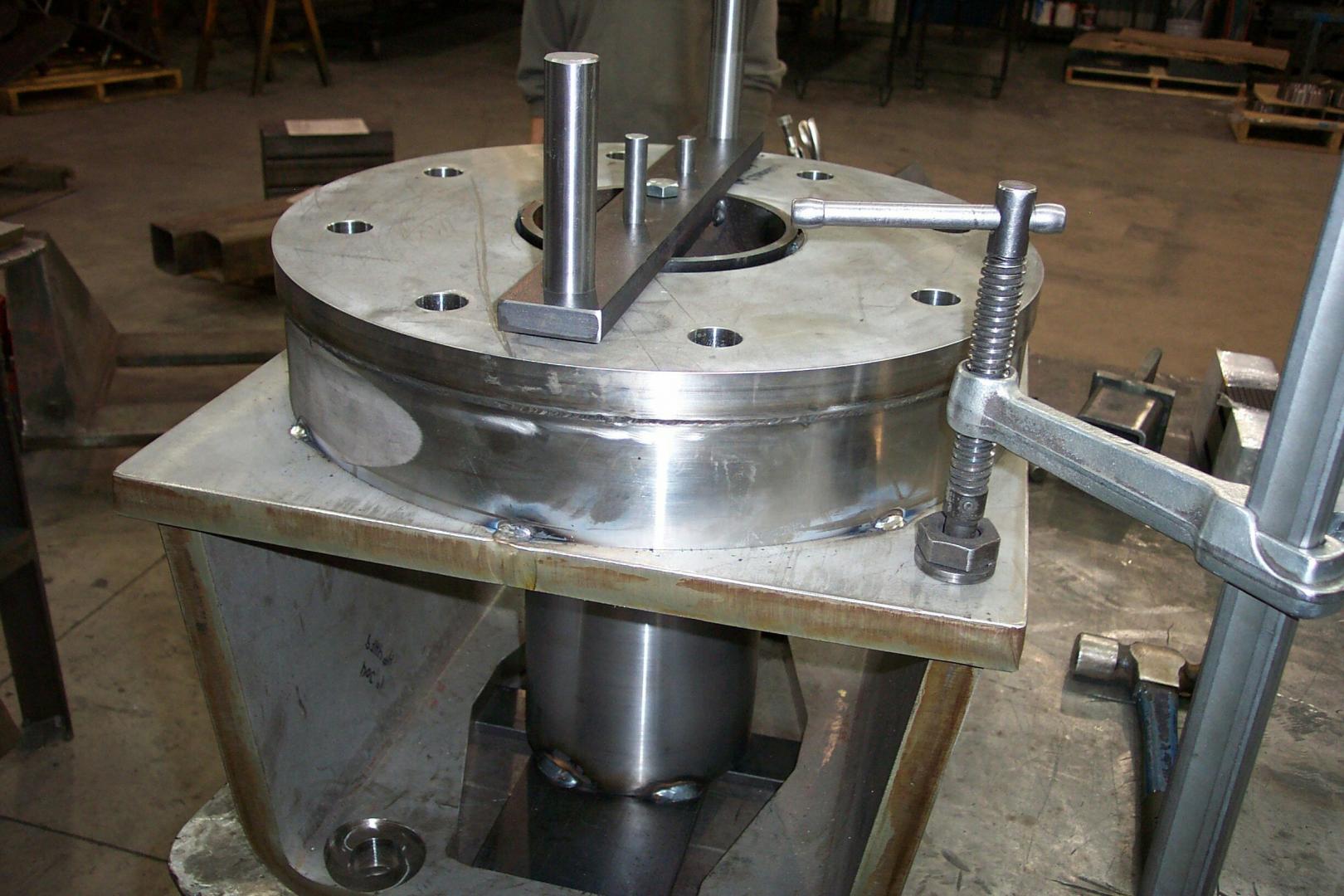 A metal flange is clamped to a workbench for fabrication in a workshop setting.