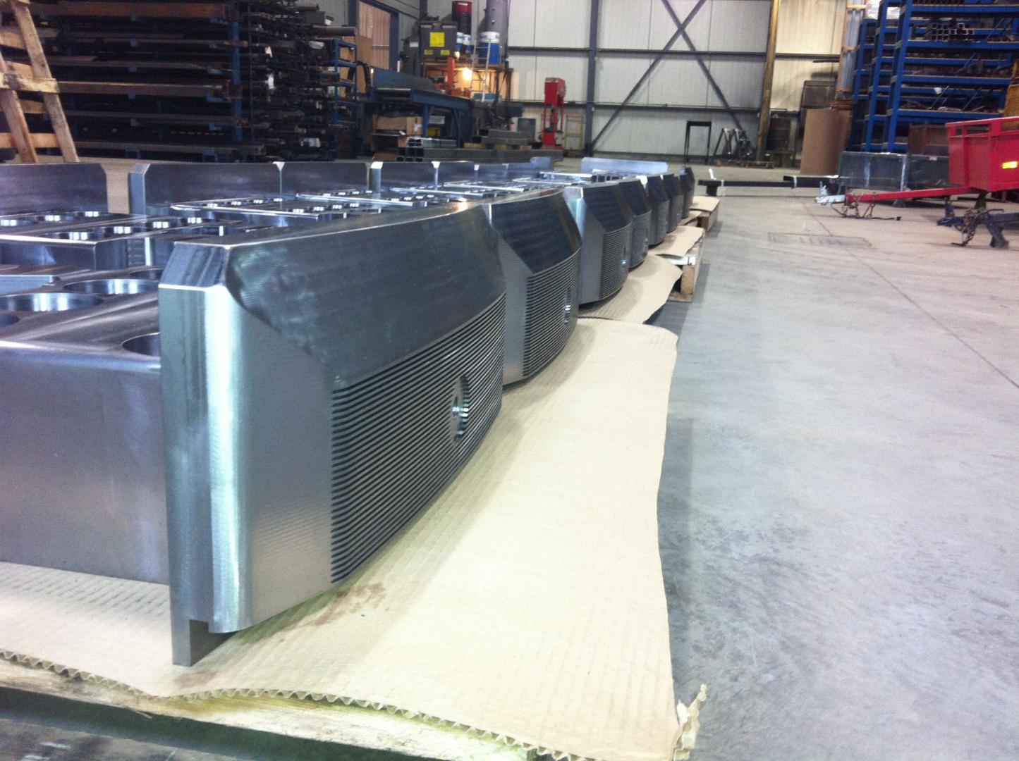 Dans un atelier, une rangée de composants industriels métalliques à façade grillagée repose sur du carton.
