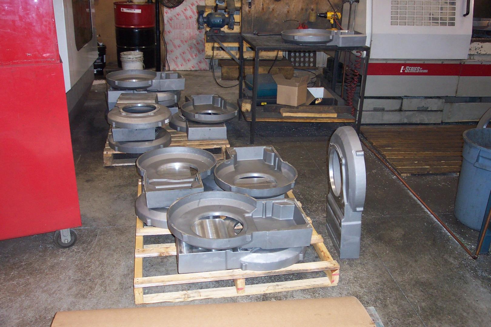 Des pièces industrielles métalliques sur des palettes en bois dans un atelier d'usinage, avec une armoire rouge et des machines industrielles à proximité.