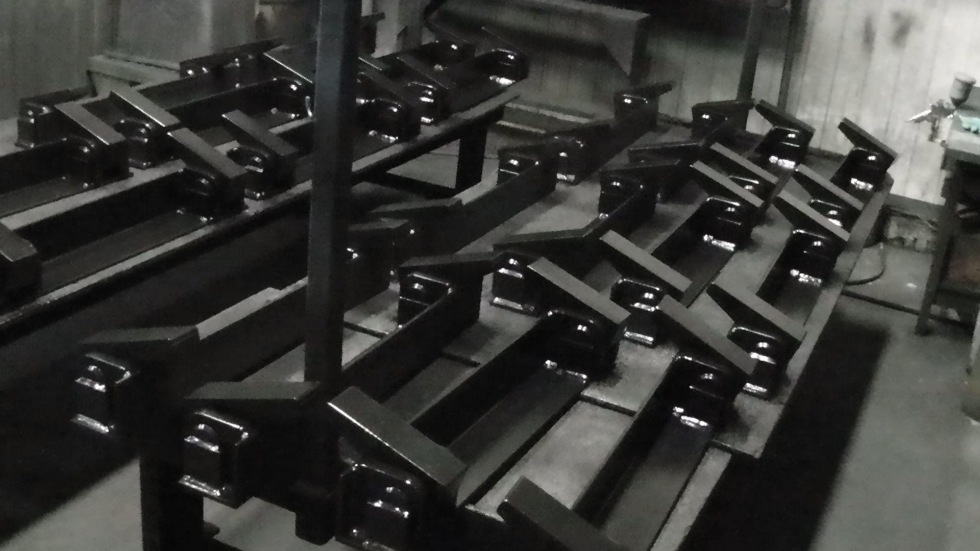 A workshop scene shows rows of finished, black-painted metal structural components arranged on a flat surface.