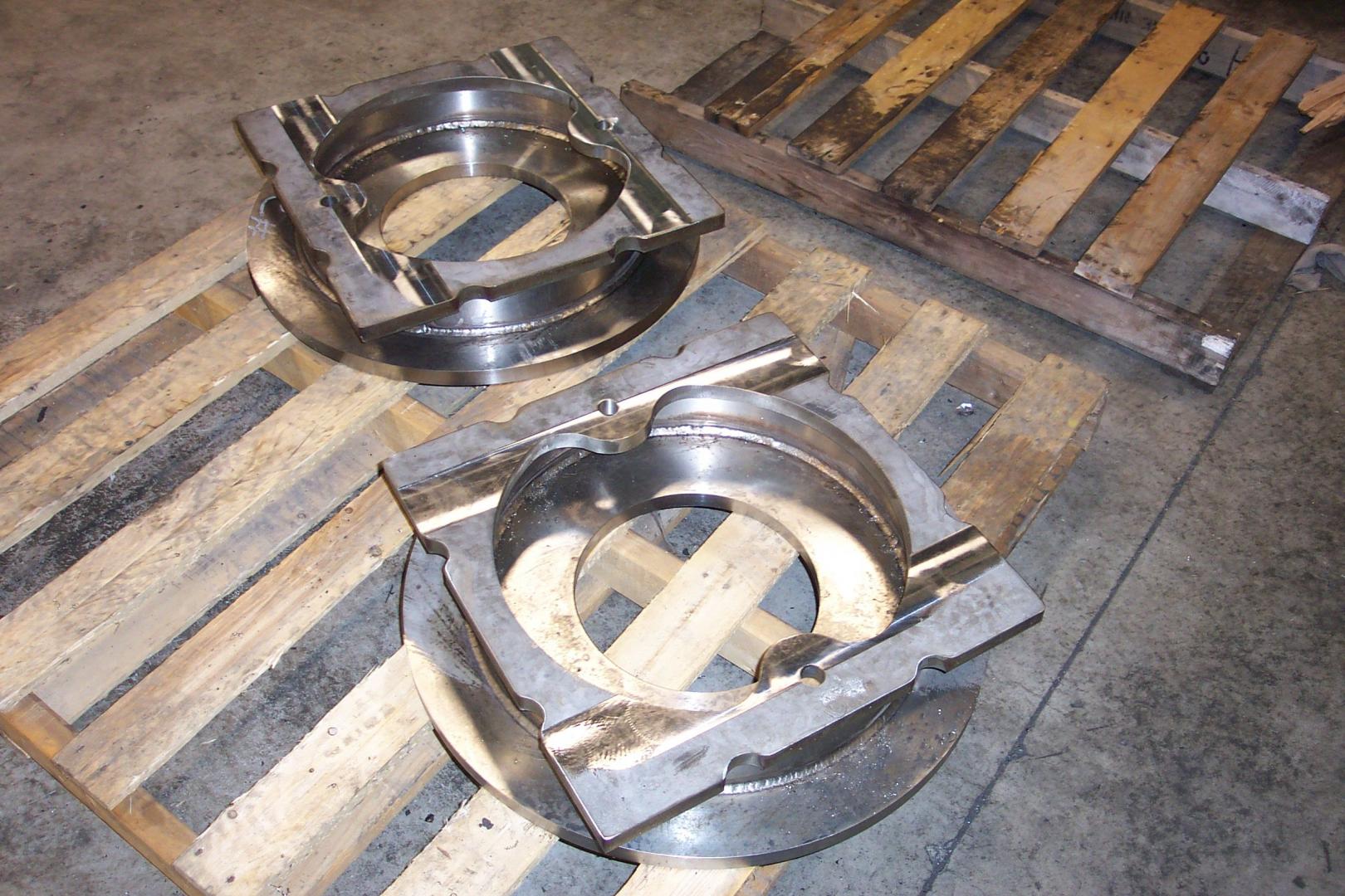 Two large, circular industrial steel components resting on wooden pallets in a workshop.