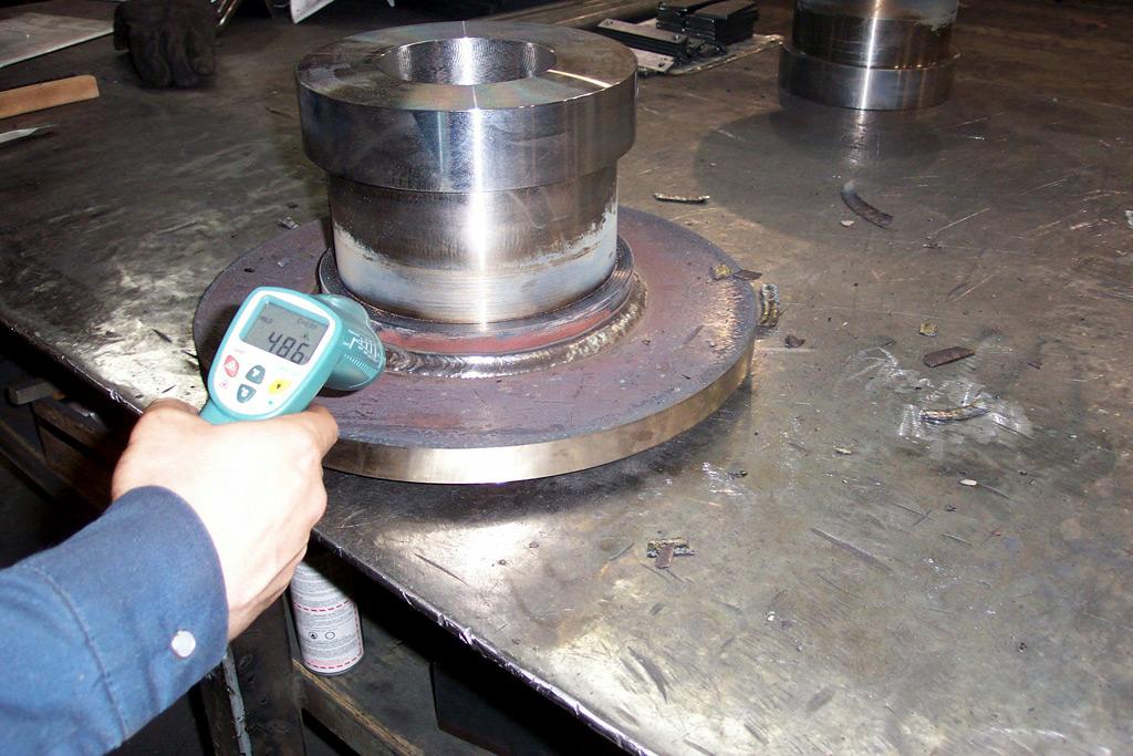 A hand uses an infrared thermometer to measure the temperature of a metal component on a workshop table.