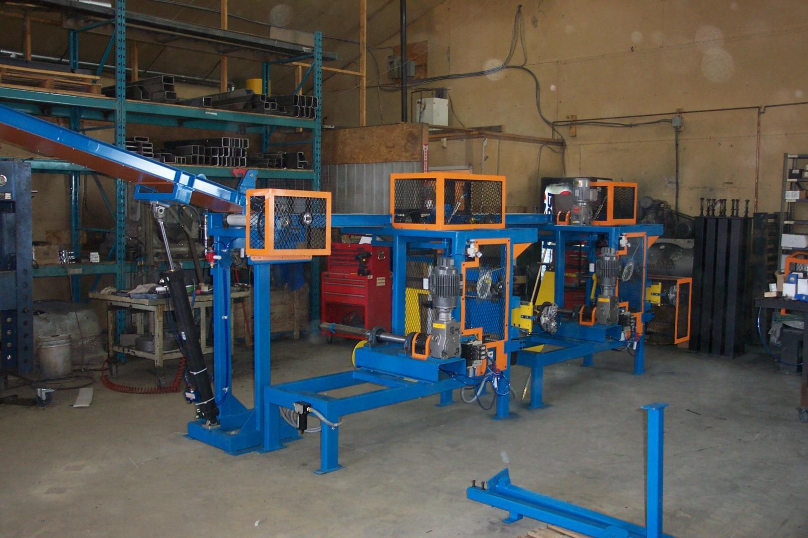 Industrial blue machinery with orange safety guards situated in a workshop with metal storage racks in the background.