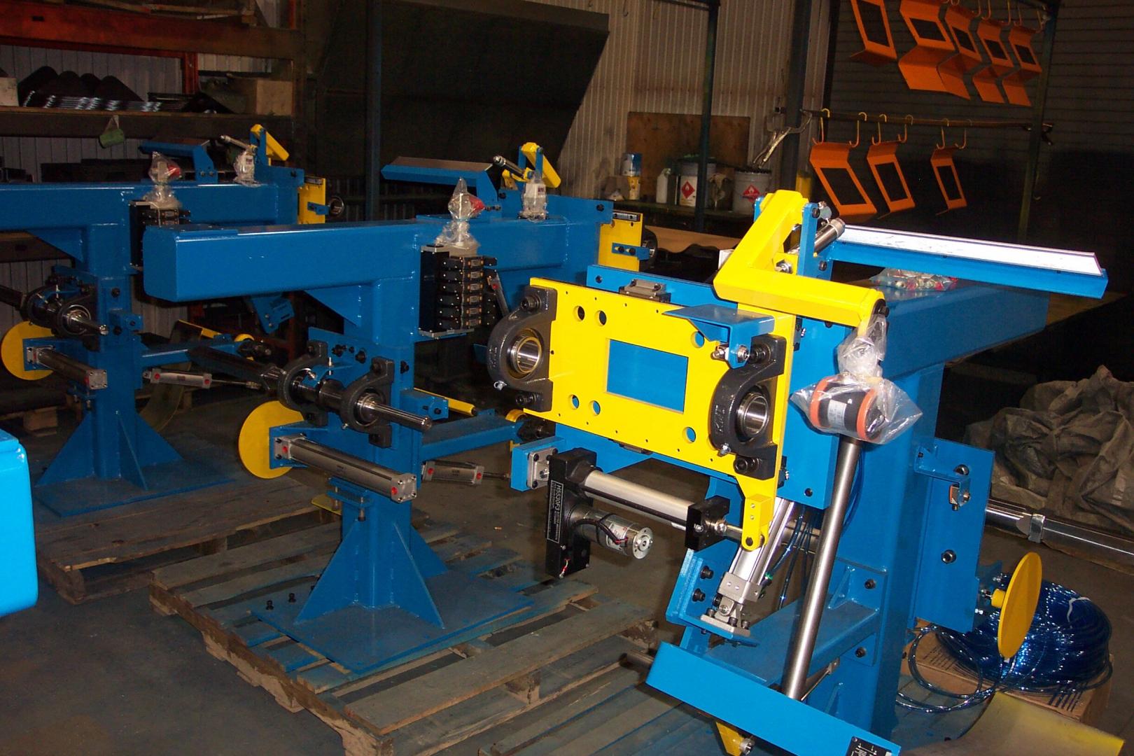 Several industrial blue and yellow metal assembly jigs sit on pallets inside a workshop.