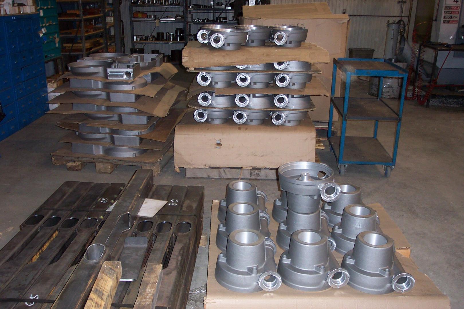 Scène d'entrepôt industriel avec des piles de pièces moulées et usinées en métal sur des palettes.