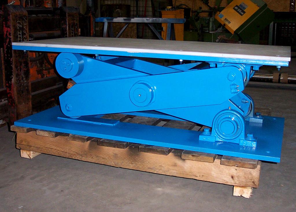 A blue industrial scissor lift table sits on a wooden pallet inside a workshop.