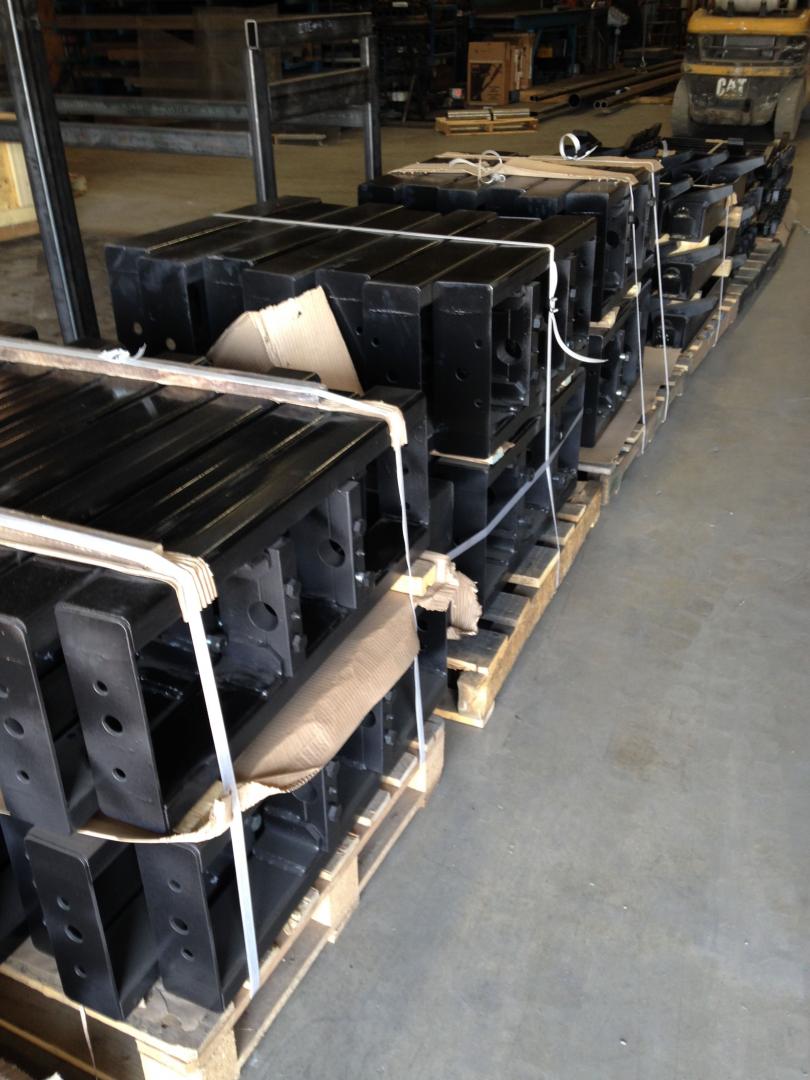 Rows of black metal machine parts stacked on wooden pallets in a warehouse.