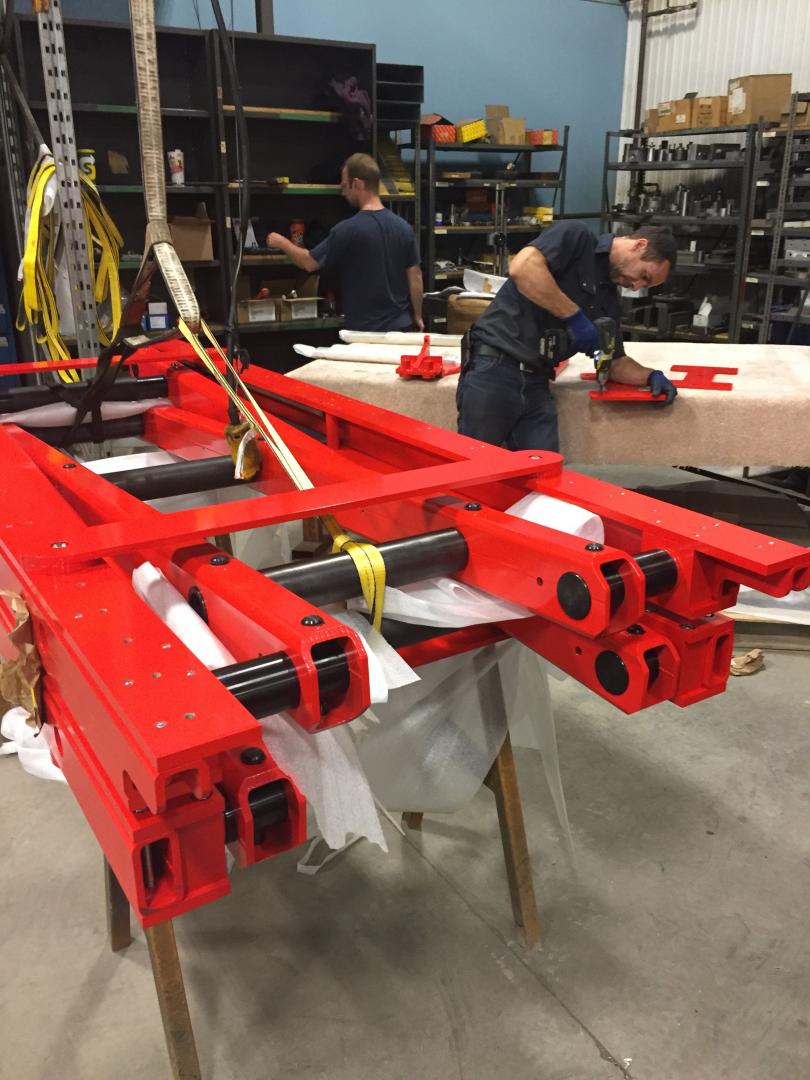 Two people working on a large red metal industrial machine in a workshop.