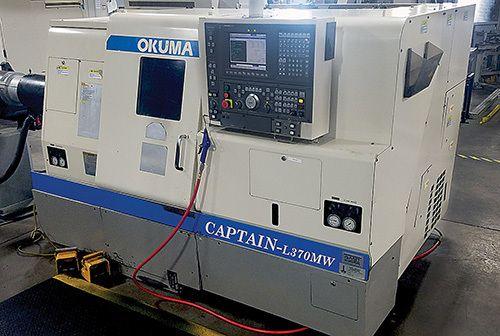 Une machine à tourner à commande numérique Okuma Captain L370MW dans un environnement industriel, de couleur blanche et bleue.
