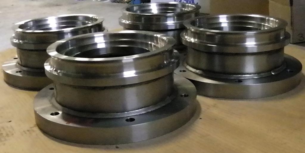 Several polished, metallic industrial pipe flanges sit on a workshop floor.