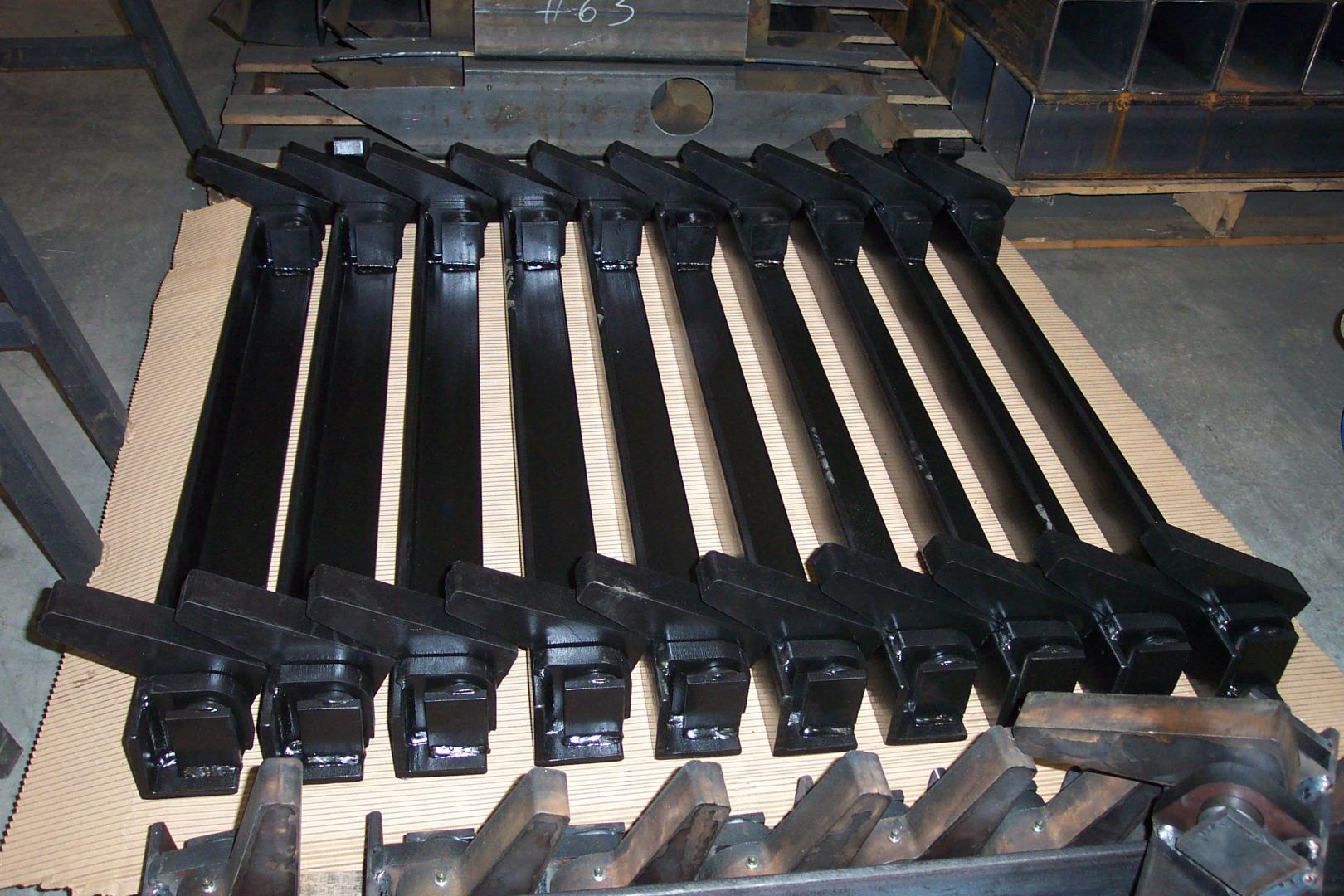 A row of black metal components arranged on a wooden pallet in a workshop or industrial storage setting.