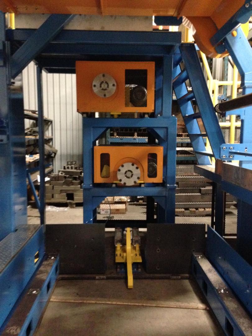 An industrial factory floor showing large, blue metal support structures holding stacked orange machinery modules.