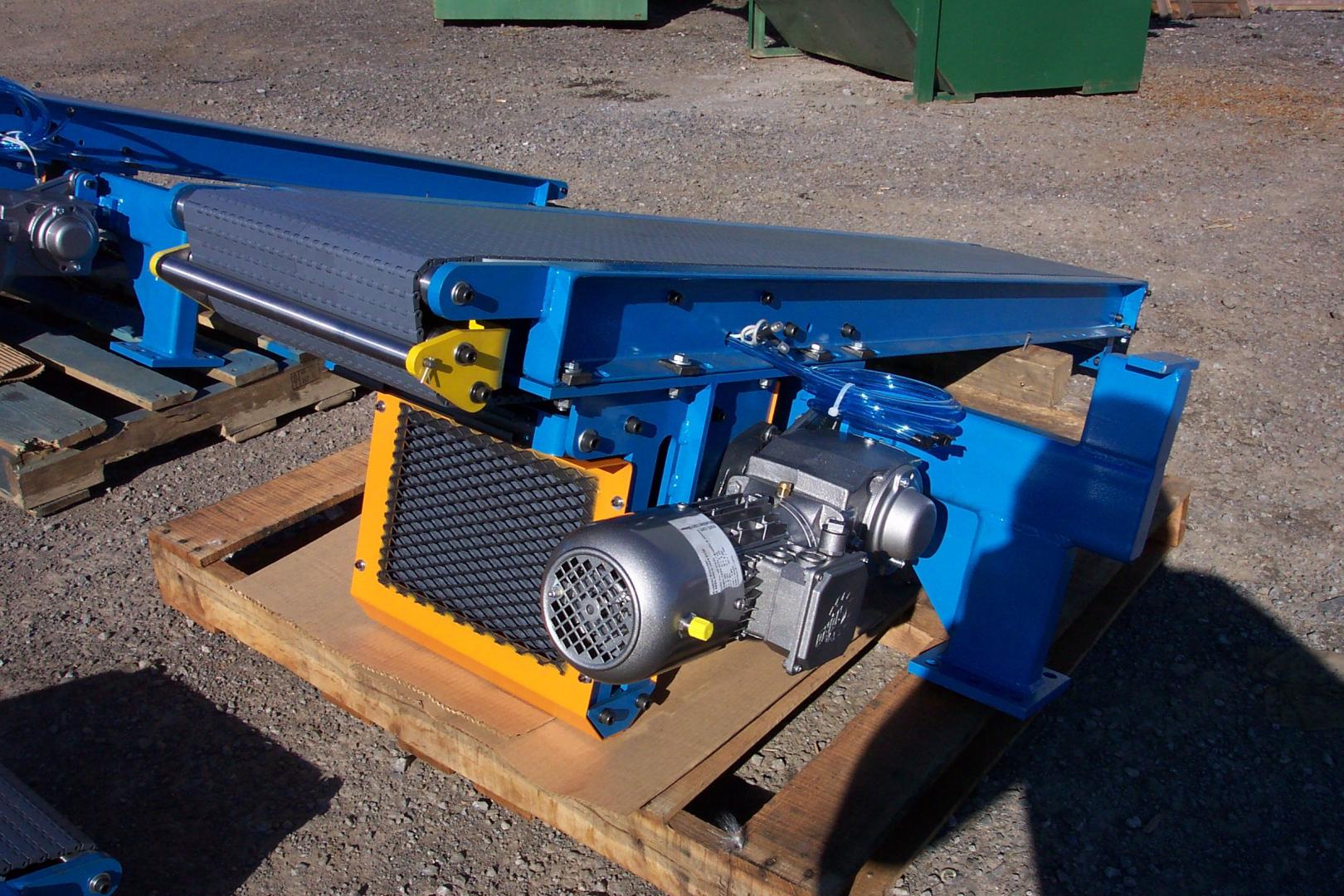 A blue industrial conveyor belt unit with an attached electric motor, sitting on a wooden pallet outdoors.
