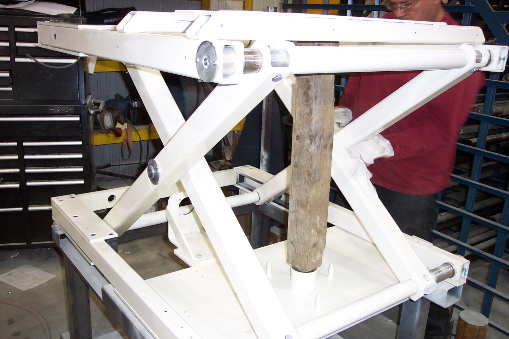 A person in a red shirt works on a white metal scissor lift table in a workshop.
