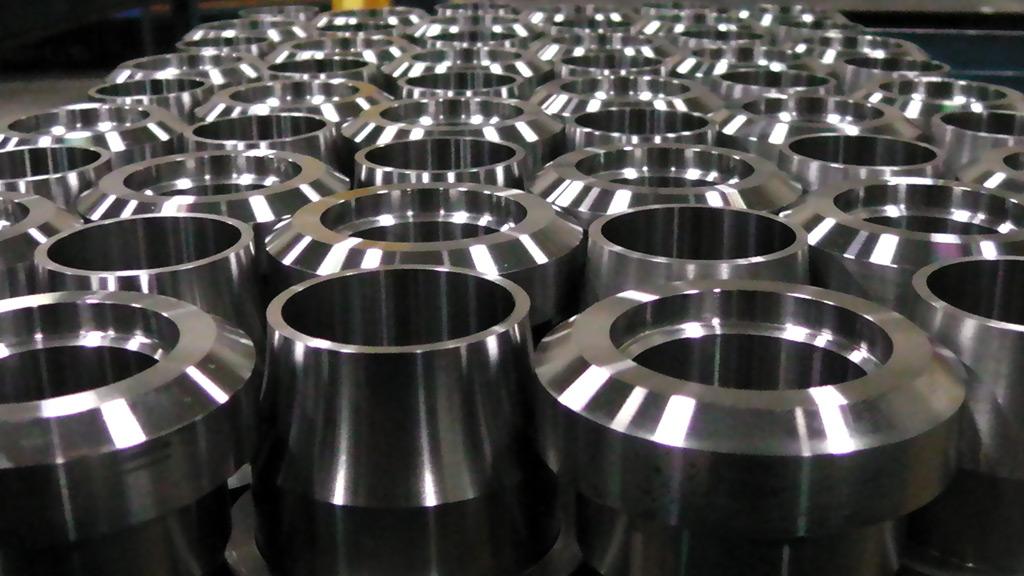 A high-angle, close-up view of numerous identical, cylindrical machined metal parts arranged in uniform rows.
