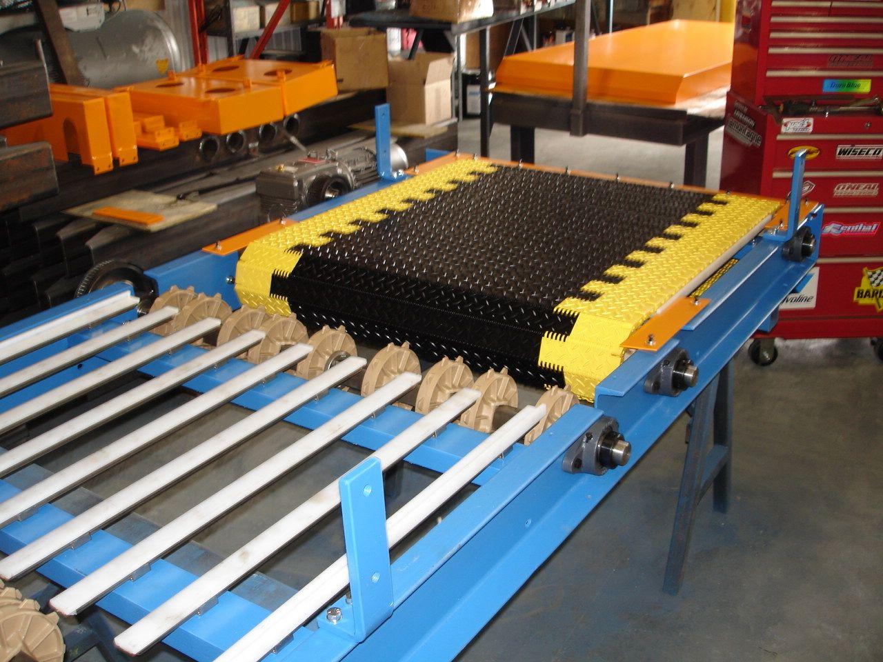 Industrial conveyor system with white plastic slats and a central yellow and black modular belt in a workshop.