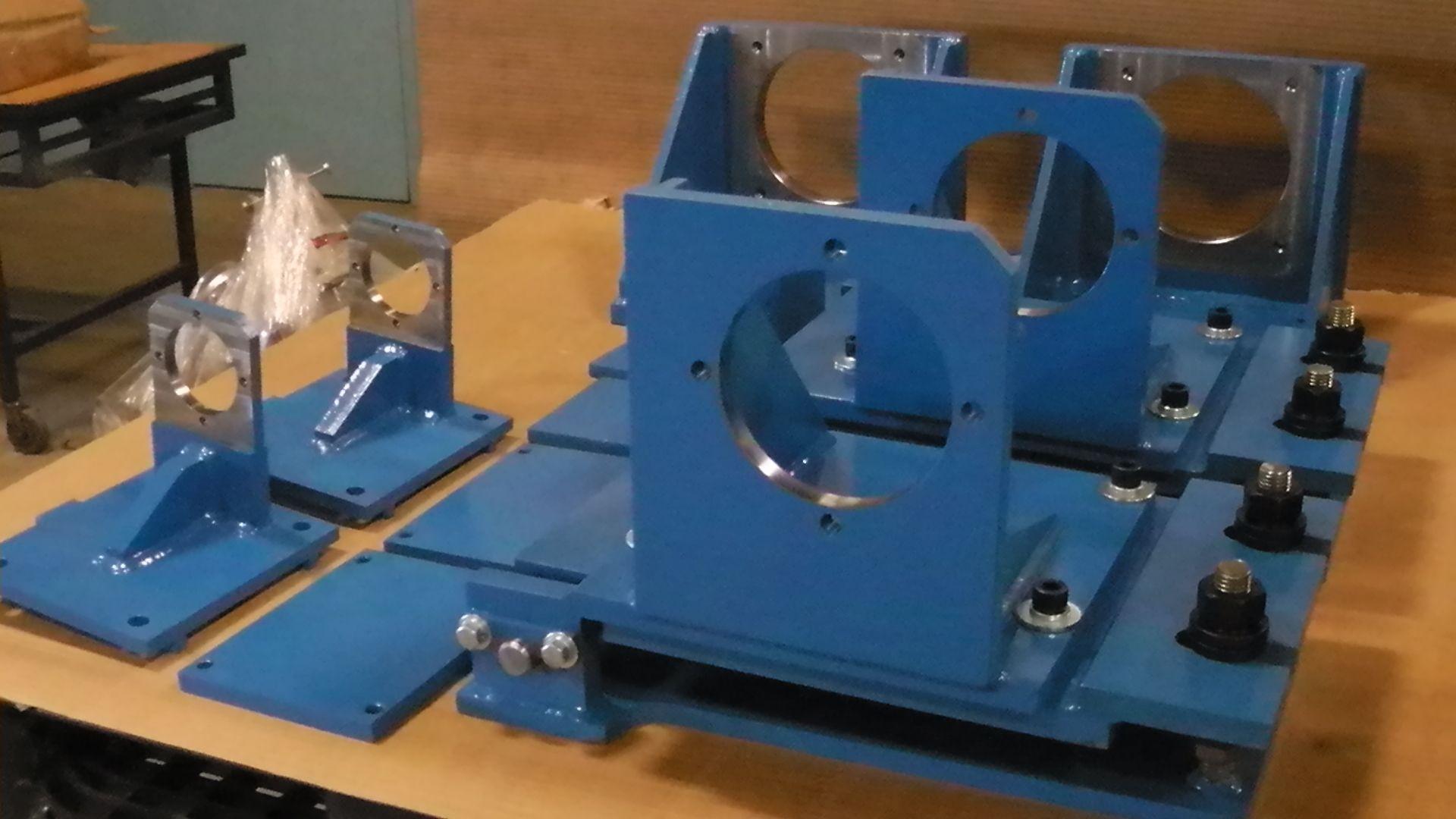 Several blue, industrial metal machine components with circular cutouts are arranged on a workbench.
