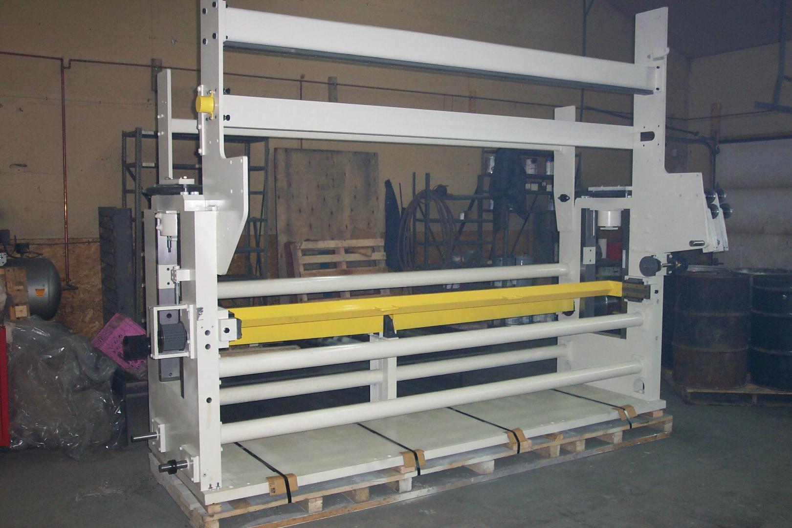 Large white industrial machinery frame with a yellow horizontal bar, standing on wooden pallets in a warehouse.