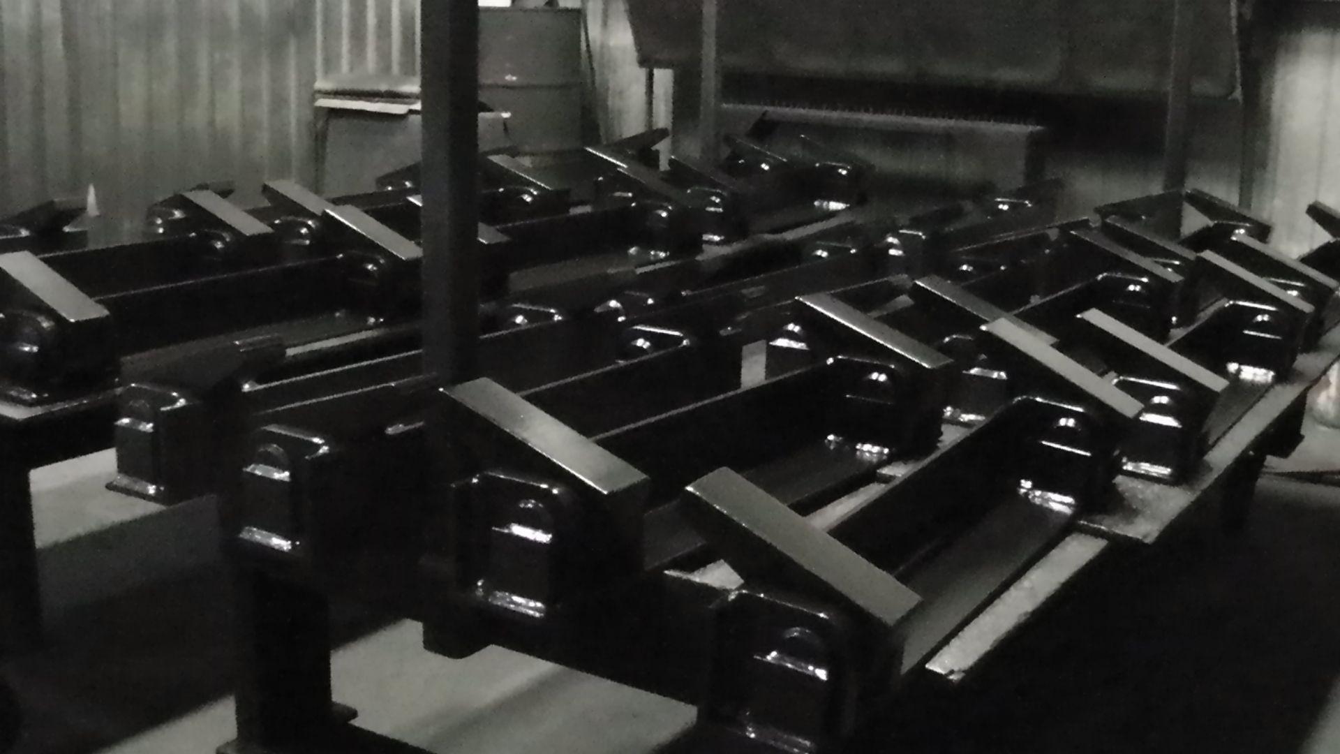 A row of identical, black painted metal industrial components arranged on a flat surface in a workshop.