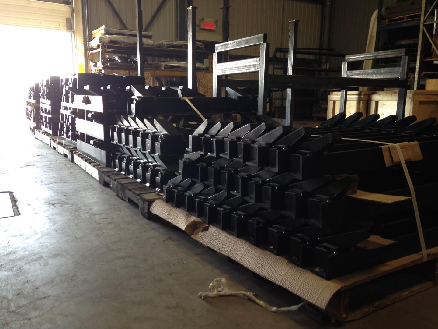 Rows of identical black industrial metal parts stacked on wooden shipping pallets inside a warehouse.