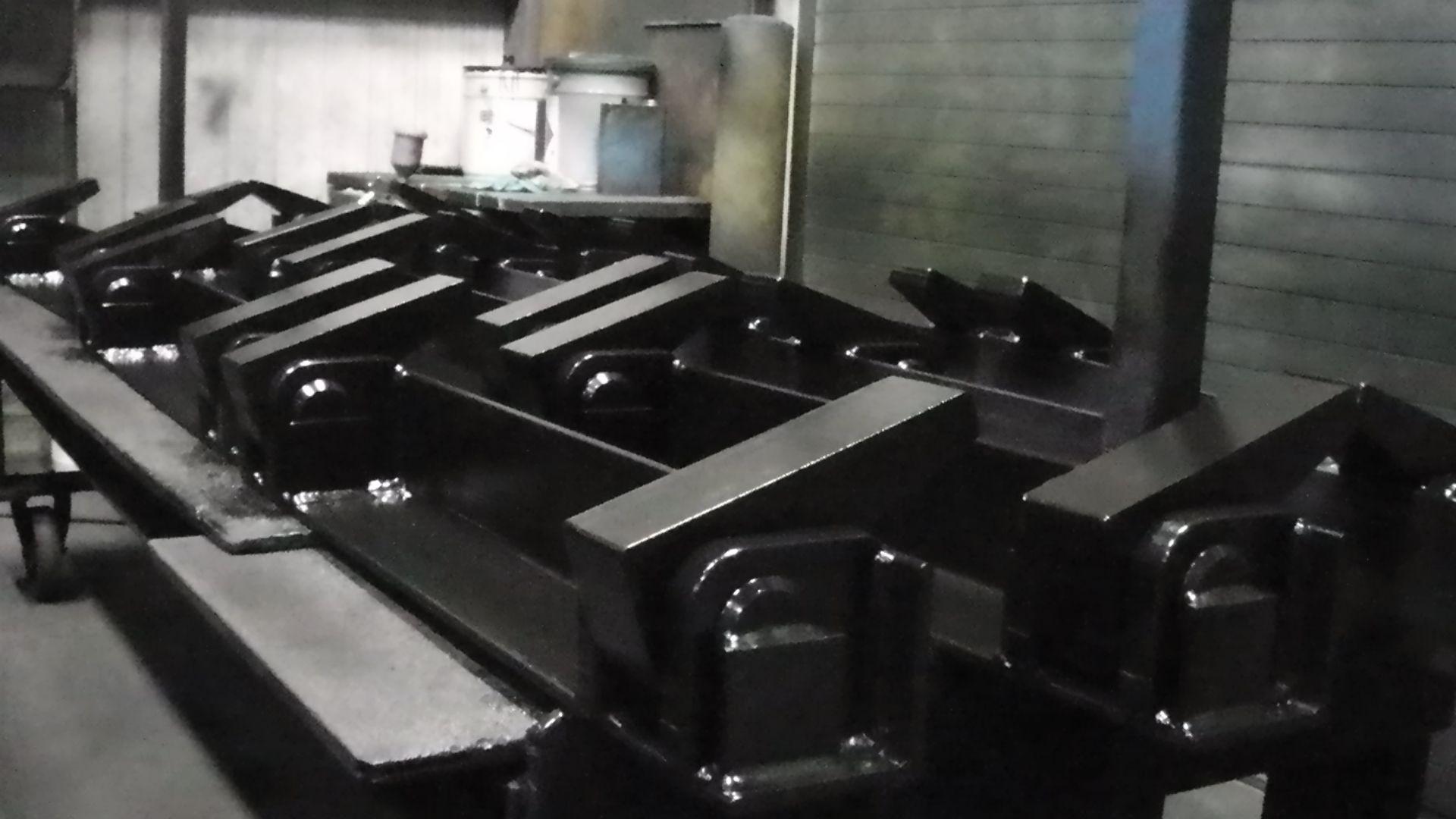 A workshop table featuring multiple identical, glossy black steel components awaiting assembly or transport.
