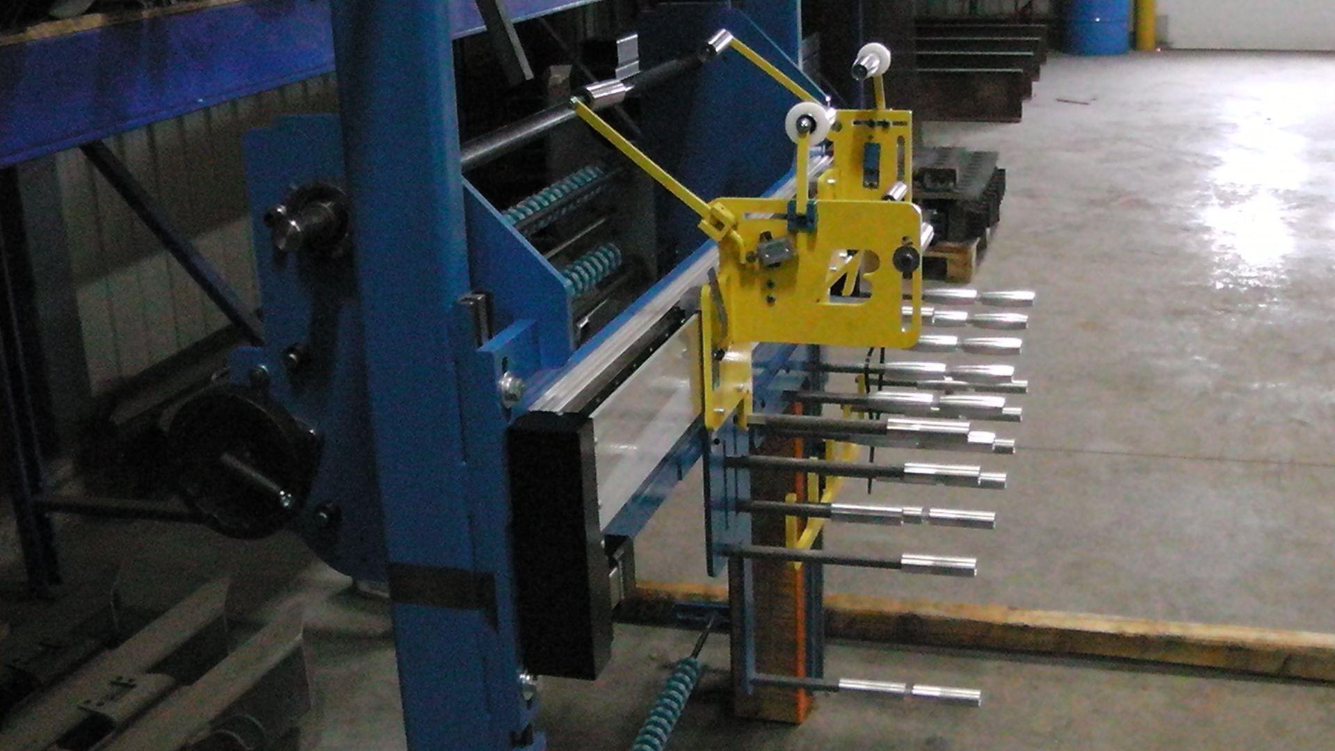 A blue industrial machine with a yellow side-mounted adjustment assembly and a row of horizontal metal rods.