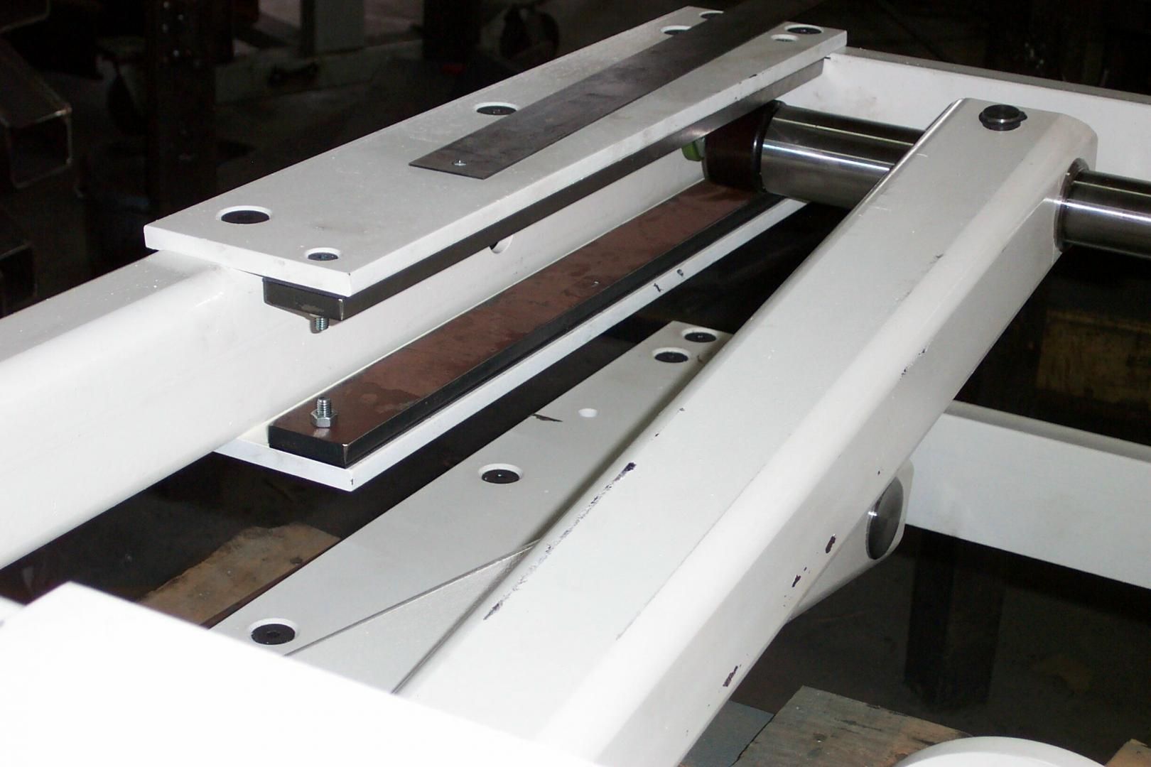 A close-up view of a white, industrial metal structure featuring a sliding mechanism and a rectangular brown block.