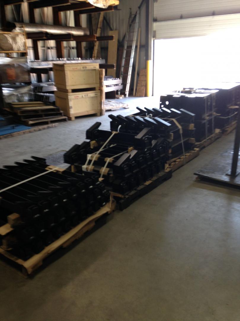 Industrial warehouse interior featuring rows of stacked black metal components on wooden pallets.