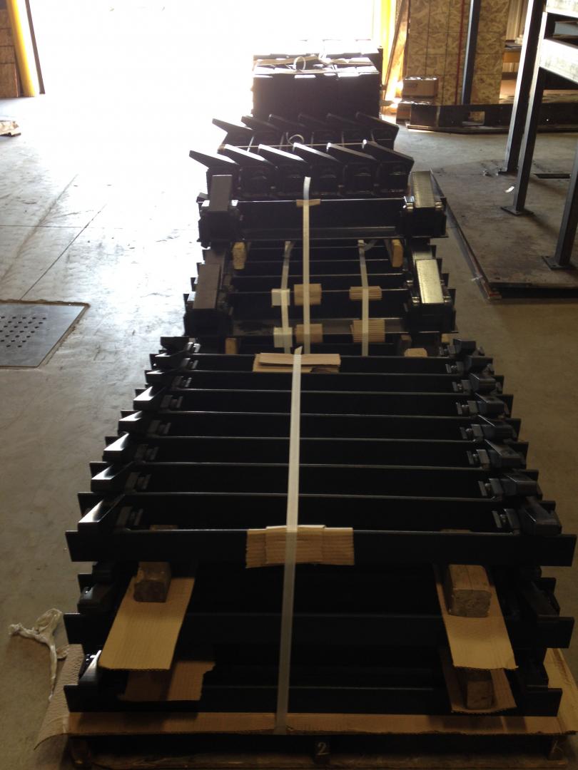 A vertical stack of black metal structural beams bundled with white plastic straps on a wooden shipping pallet.