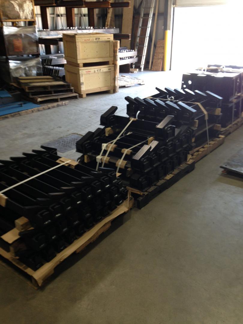 Two wooden pallets loaded with rows of black industrial metal components sit on a concrete floor in a warehouse.